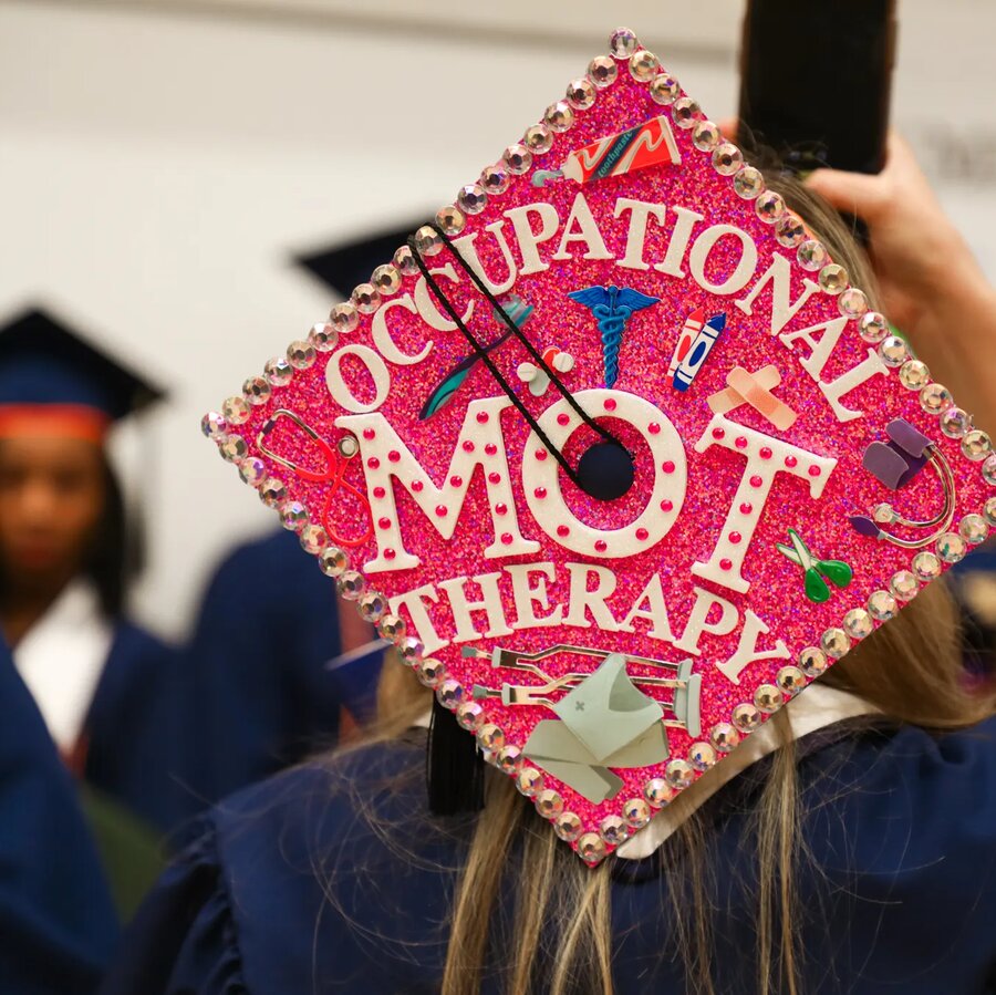 Graduate wearing graduation cap with Master of Occupational Therapy on it in colorful text