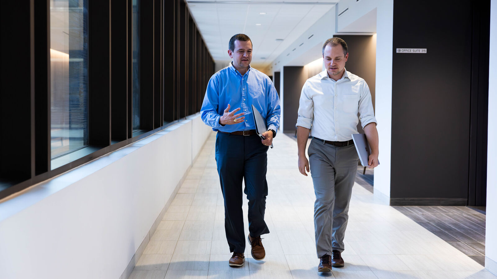 Two male Master of Health Administration Students walk through the Soules College of Business with laptops at The University of Texas at Tyler