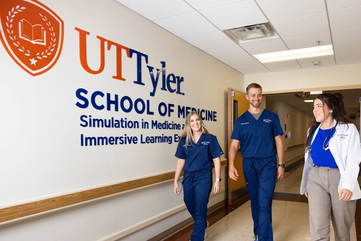 Students walk down a hall with a UT Tyler School of Medicine logo on the wall