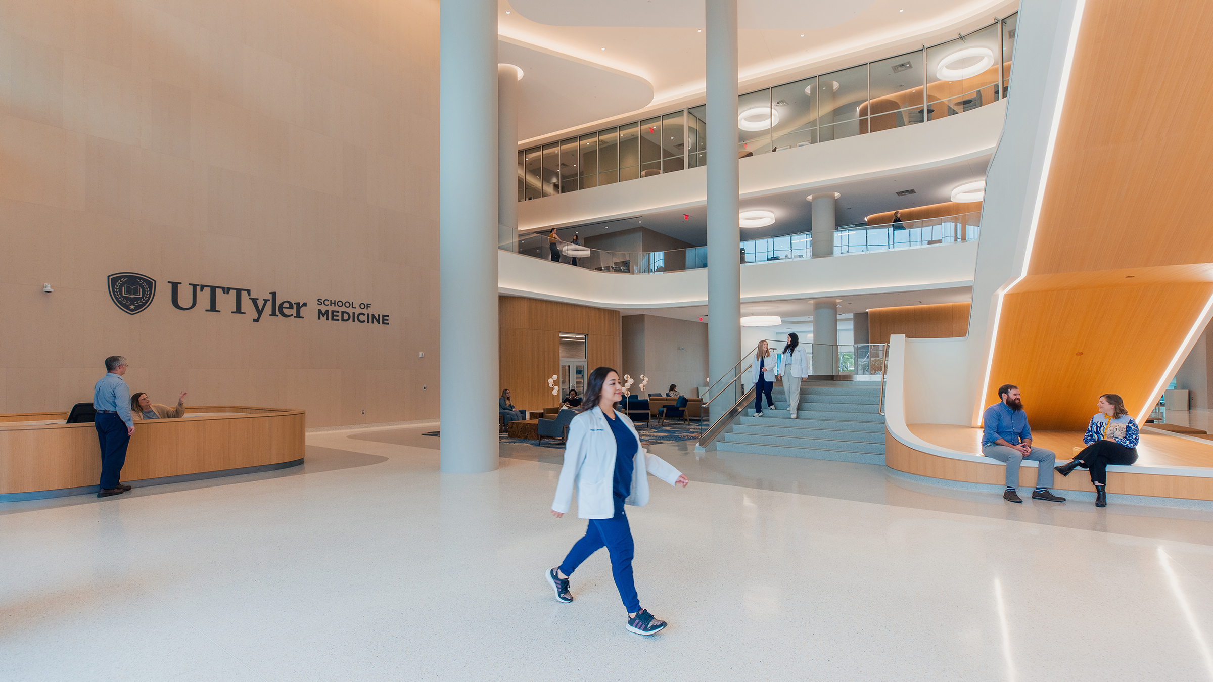 Student in white coat walking across School of Medicine lobby.