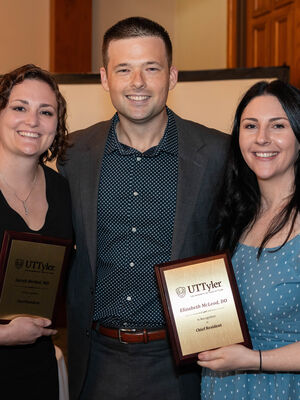 three people smiling and holding plaques at a graduation