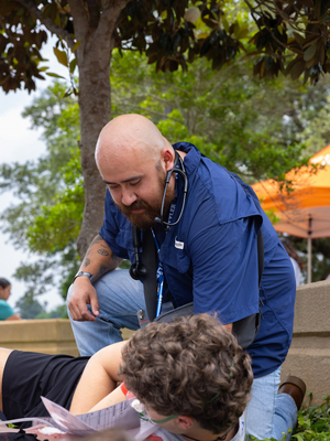 Abram Garcia, UT Tyler Nursing Student, kneels over a simulated patient actor outside as he participates in a mass casualty simulation.
