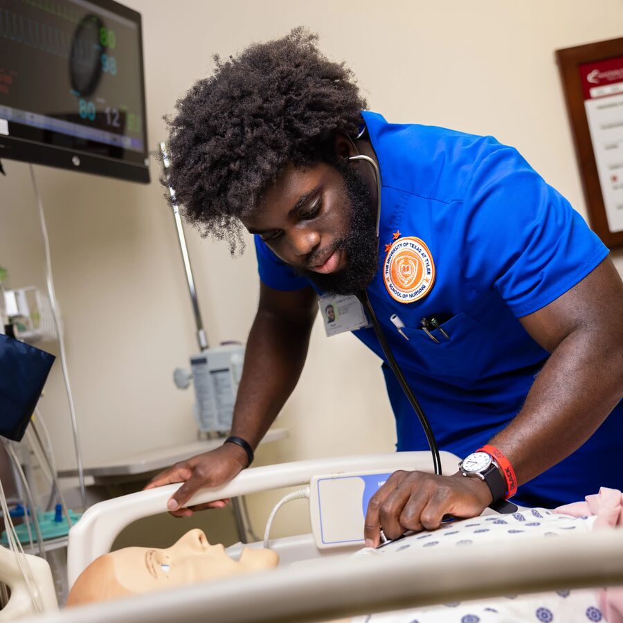 A male nursing student with a stethoscope checking a patient in a simulation room