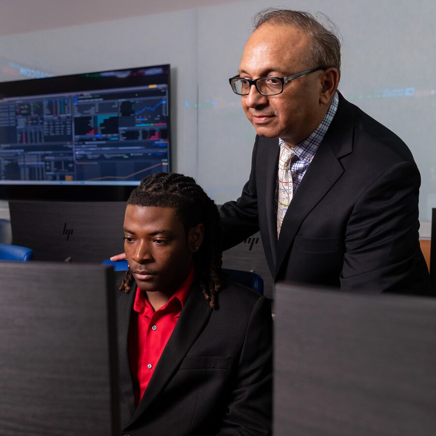 A UT Tyler faculty member looking over a student's shoulder at a computer screen in a classroom