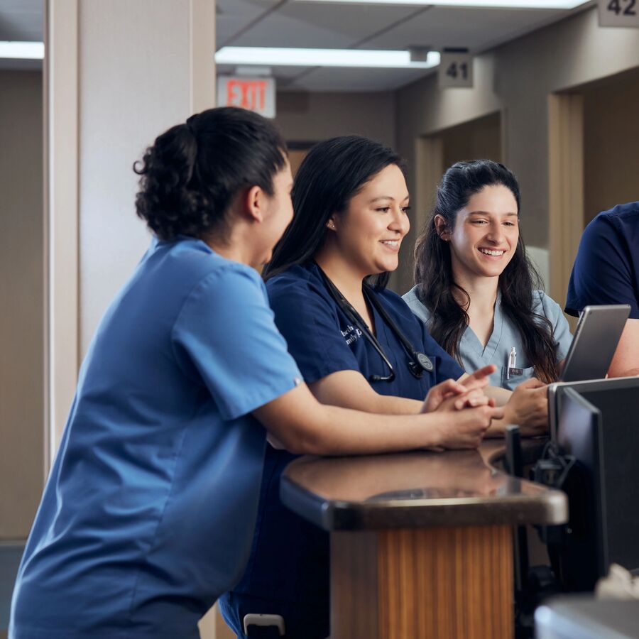 UT Tyler health sciences students wearing medical scrubs having a conversation at a nurses station.