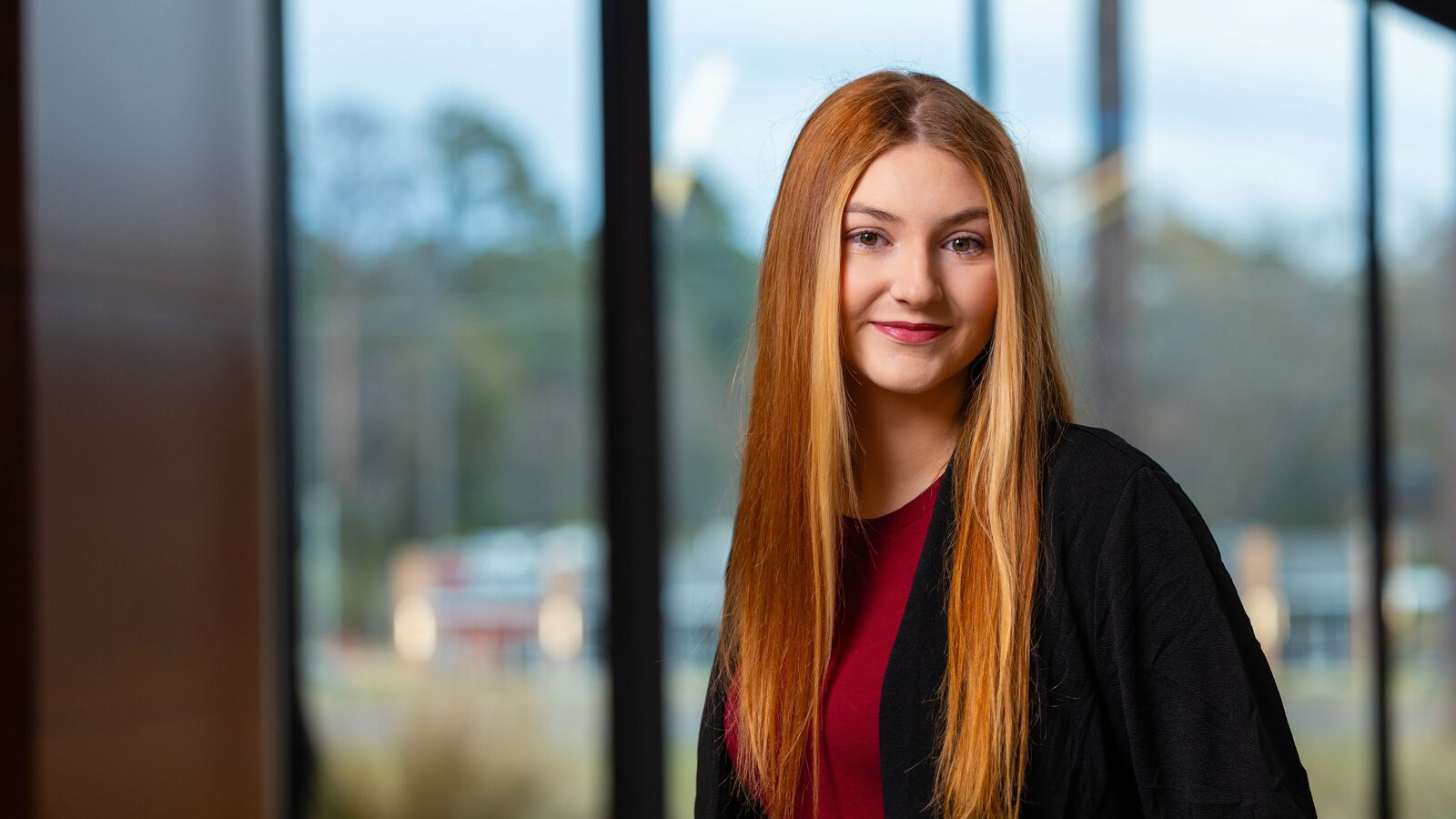 Female UT Tyler student posing in front of a row of large windows with the campus in the background