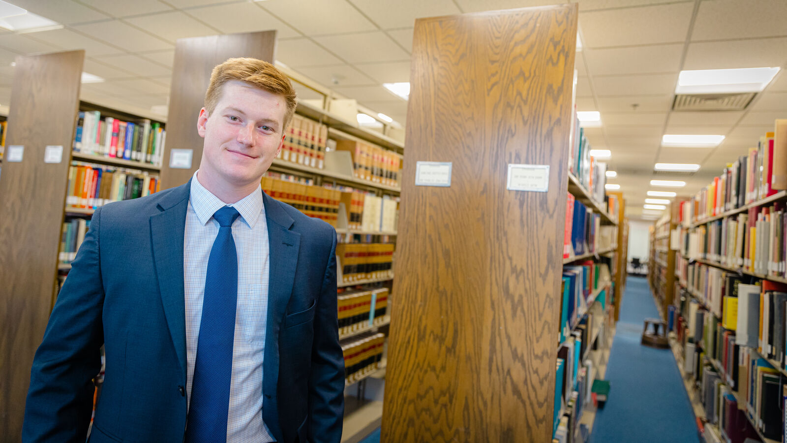 A political science student wearing a suit stands in UT Tyler's library