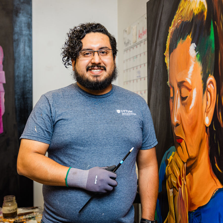 A male student in UT Tyler's BA in art program stands in front of a painting