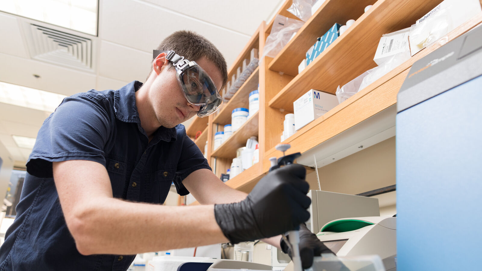 A male BS in Chemistry student at UT Tyler wearing safety glasses and gloves takes samples in a lab