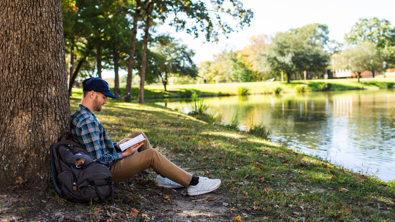 A male communication sciences and disorders student reads outdoors by the lake at The University of Texas at Tyler