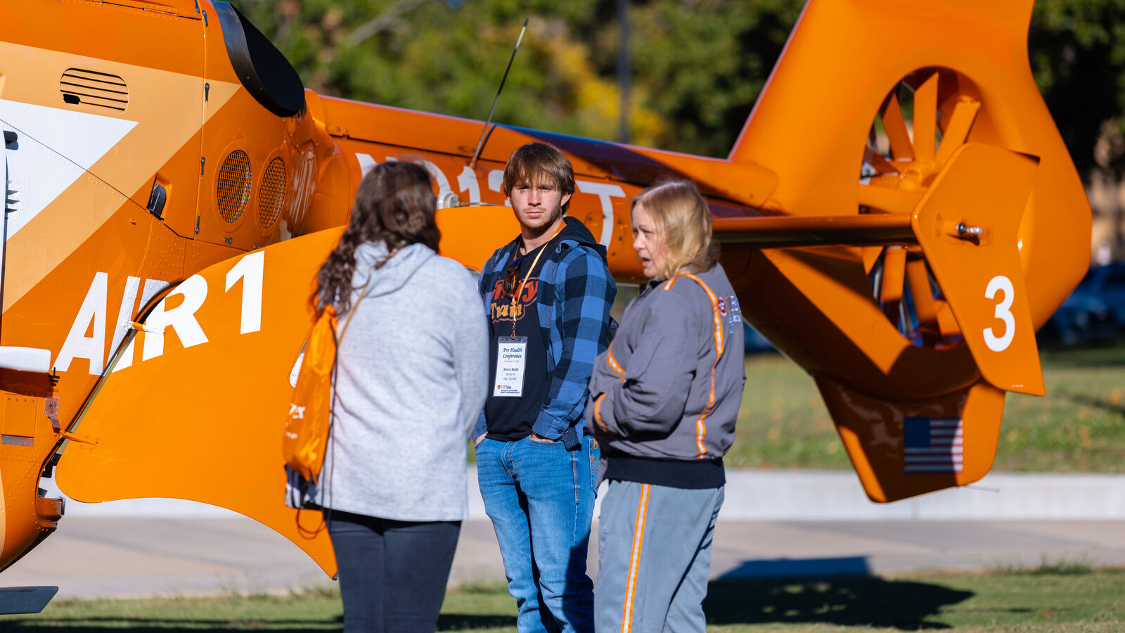 Three UT Tyler students stand outdoors near an air ambulance during the Pre-Health Student Conference.