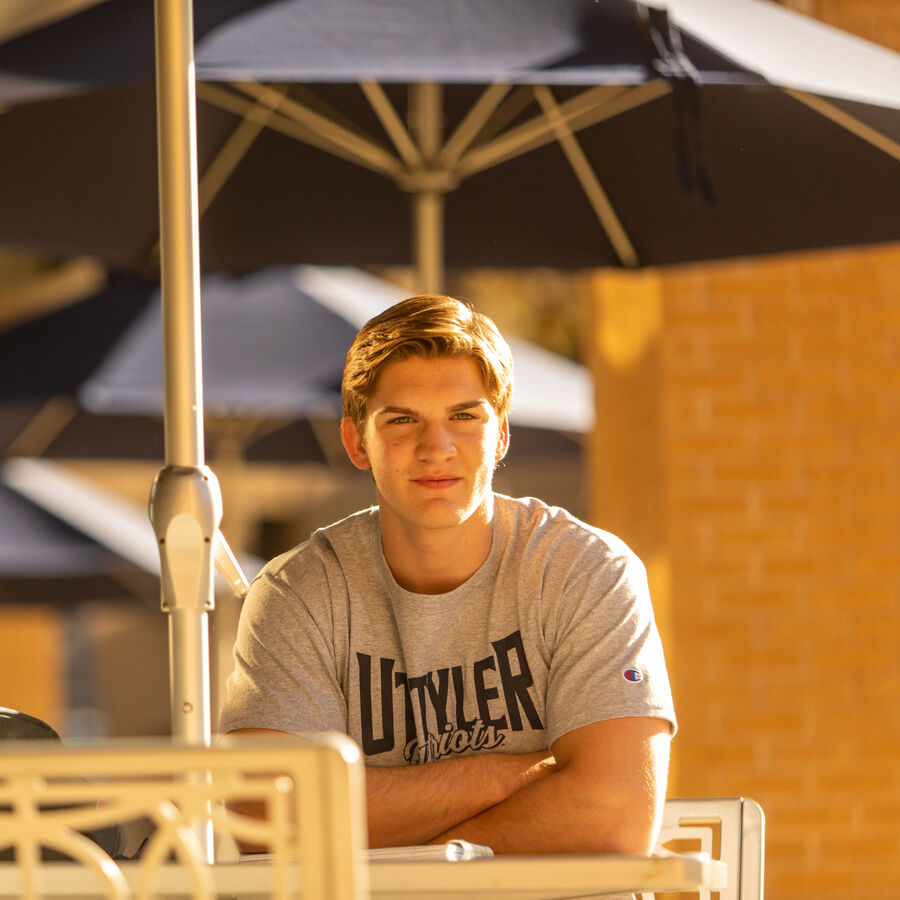 A male BSW student sits by a table outside UT Tyler's University Center