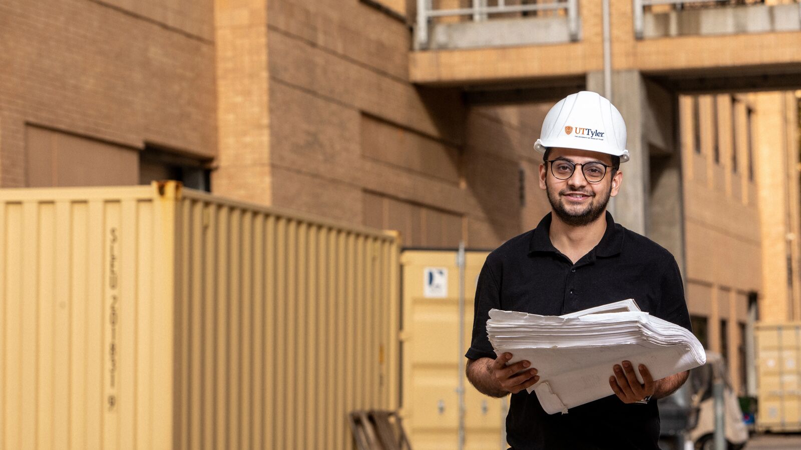 A UT Tyler construction management major stands in front of a project in the field