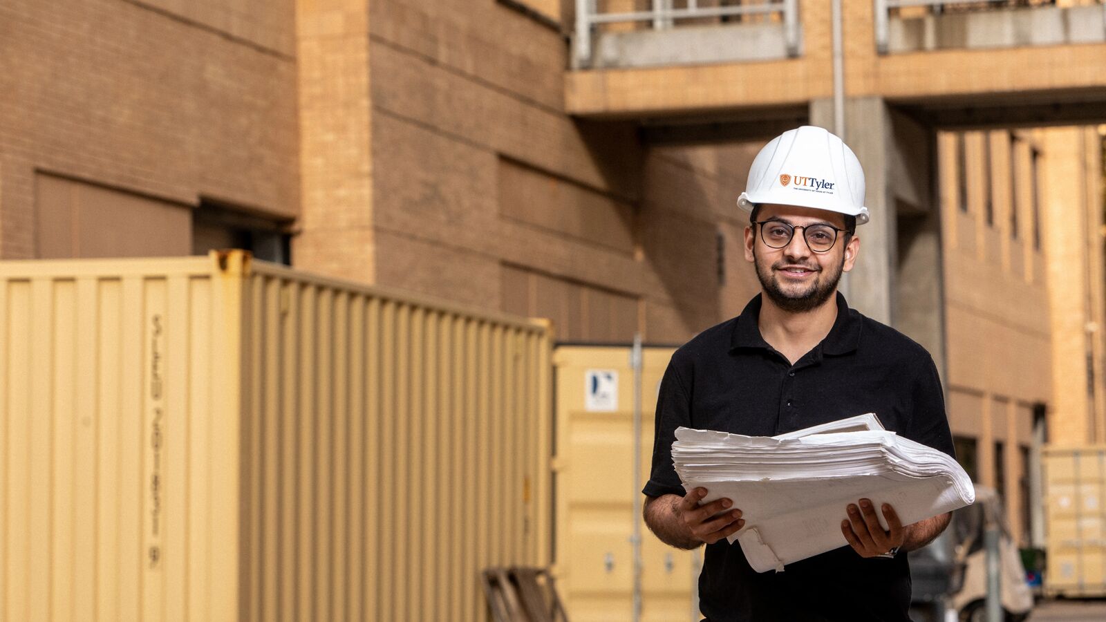 A UT Tyler construction management major stands in front of a project in the field 