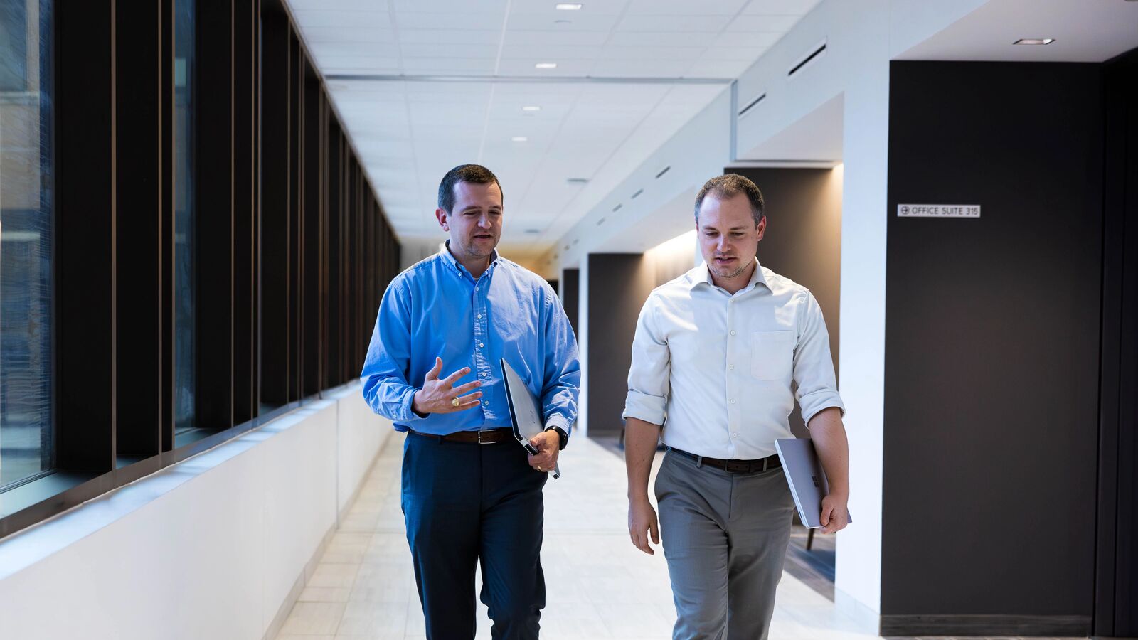Two male Master of Health Administration Students walk through the Soules College of Business with laptops at The University of Texas at Tyler