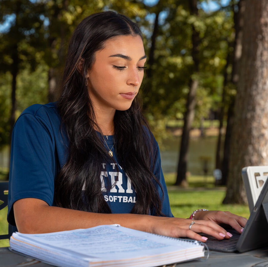 A female clinical psychology students works on a laptop outdoors at UT Tyler