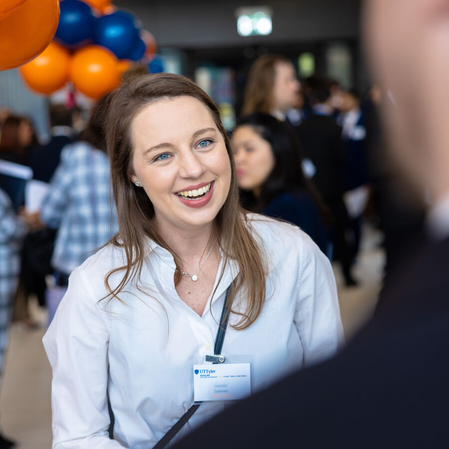 A business student smiling and talking at a networking event at UT Tyler Longview University Center