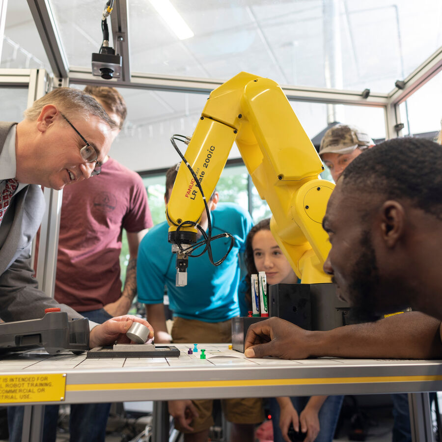 A faculty member shows students a robot arm in one of UT Tyler's industrial engineering labs.