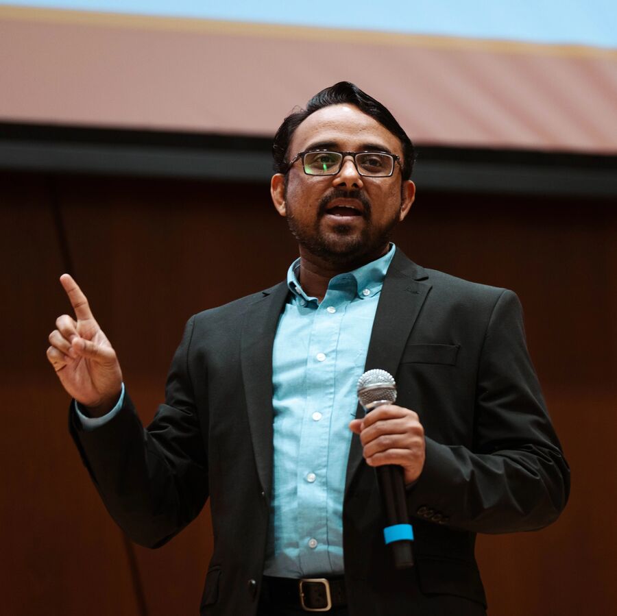 A faculty member holding a microphone and standing in front of a screen lectures a class of graduate students at The University of Texas at Tyler