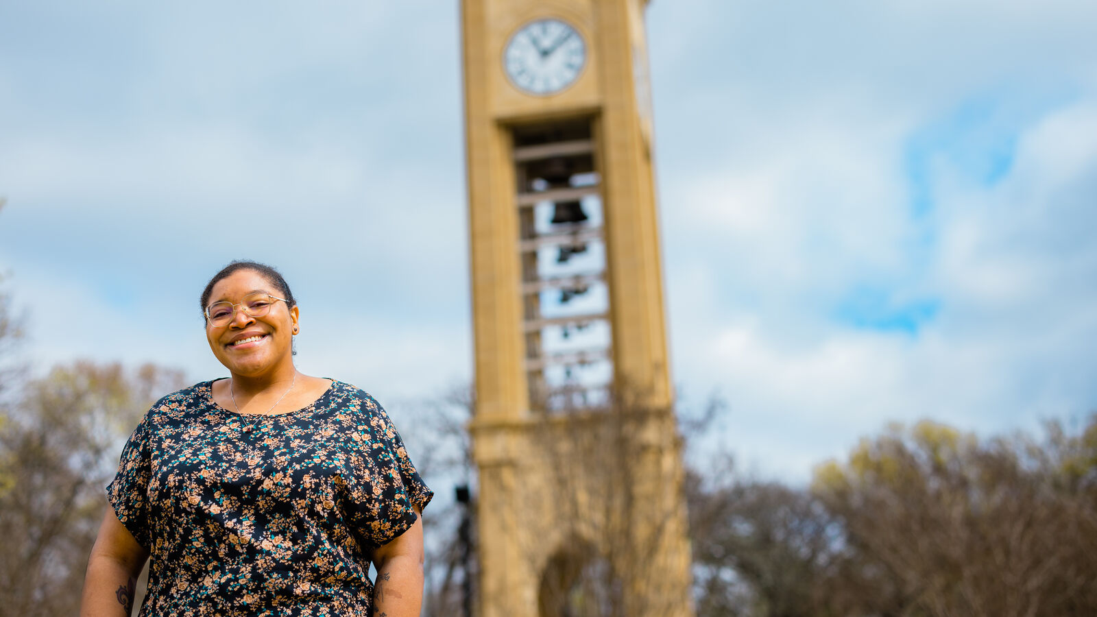 A female graduate student stands near the Bell Tower on UT Tyler's campus
