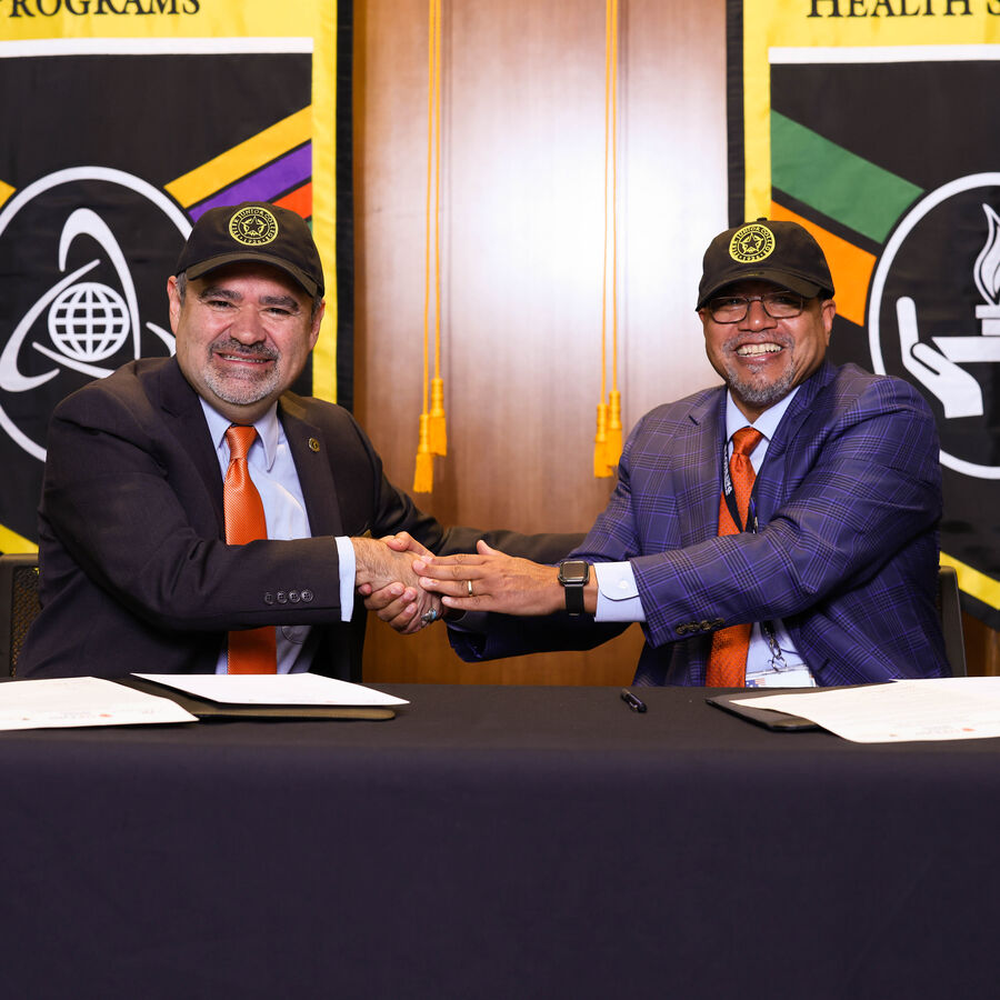 Two officials shake hands during a document signing for a promise agreement between UT Tyler and Tyler Junior College