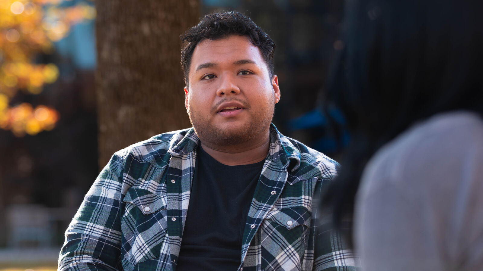 Two students talk outdoors around a table in fall at The University of Texas at Tyler