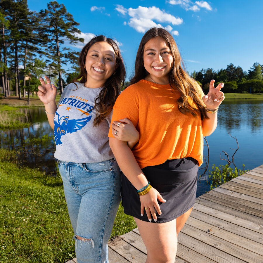 Two female students smile outdoors by the water on UT Tyler's campus