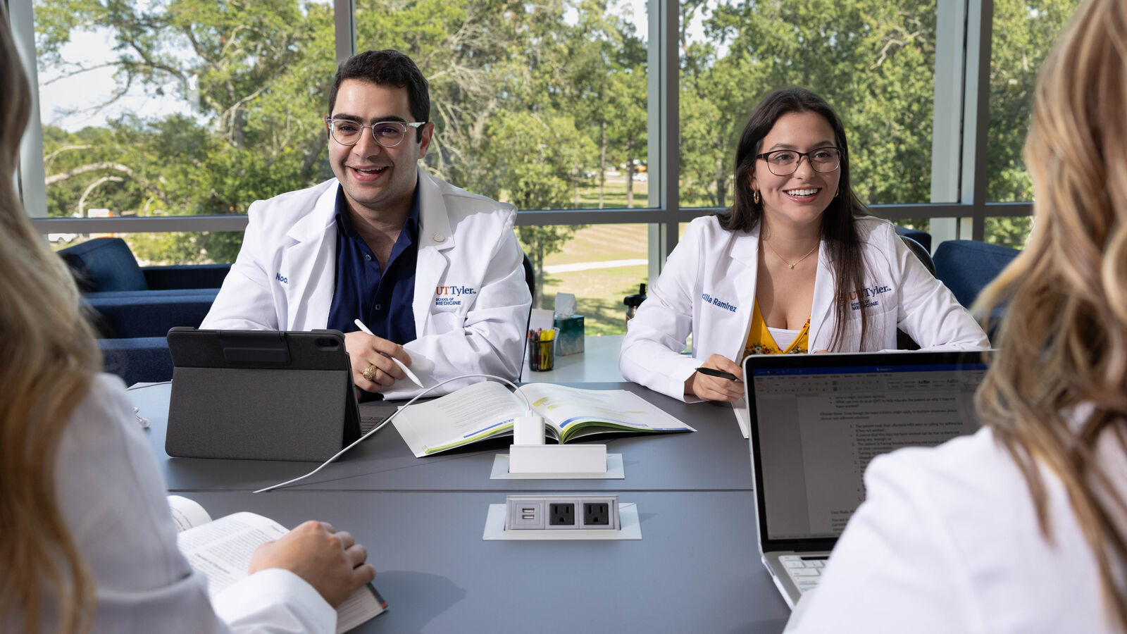 UT Tyler School of Medicine students in lab coats sit around a table with laptops