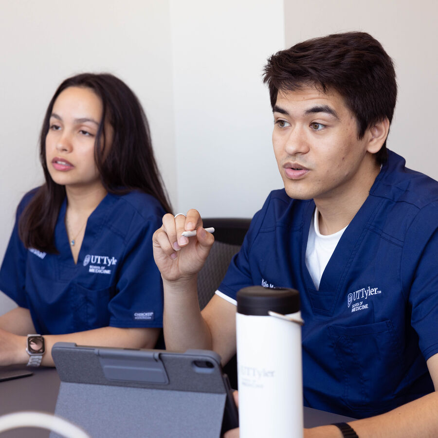 UT Tyler School of Medicine students in scrubs sit around a table discussing research