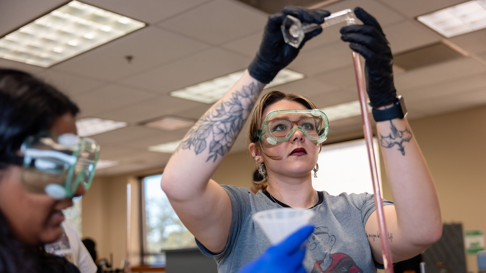 A BS in Chemistry student at UT Tyler wearing safety glasses and gloves takes samples in a lab