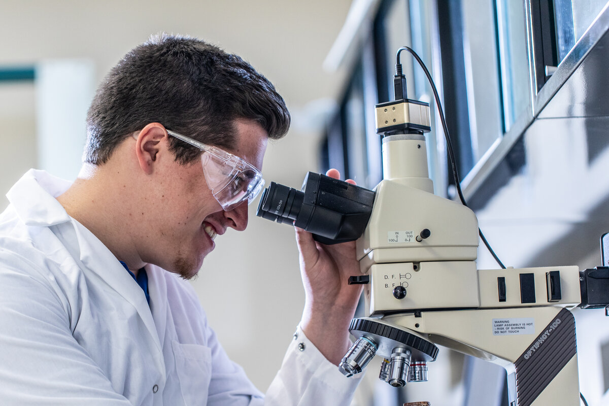 Student in a lab coat looking down a microscope