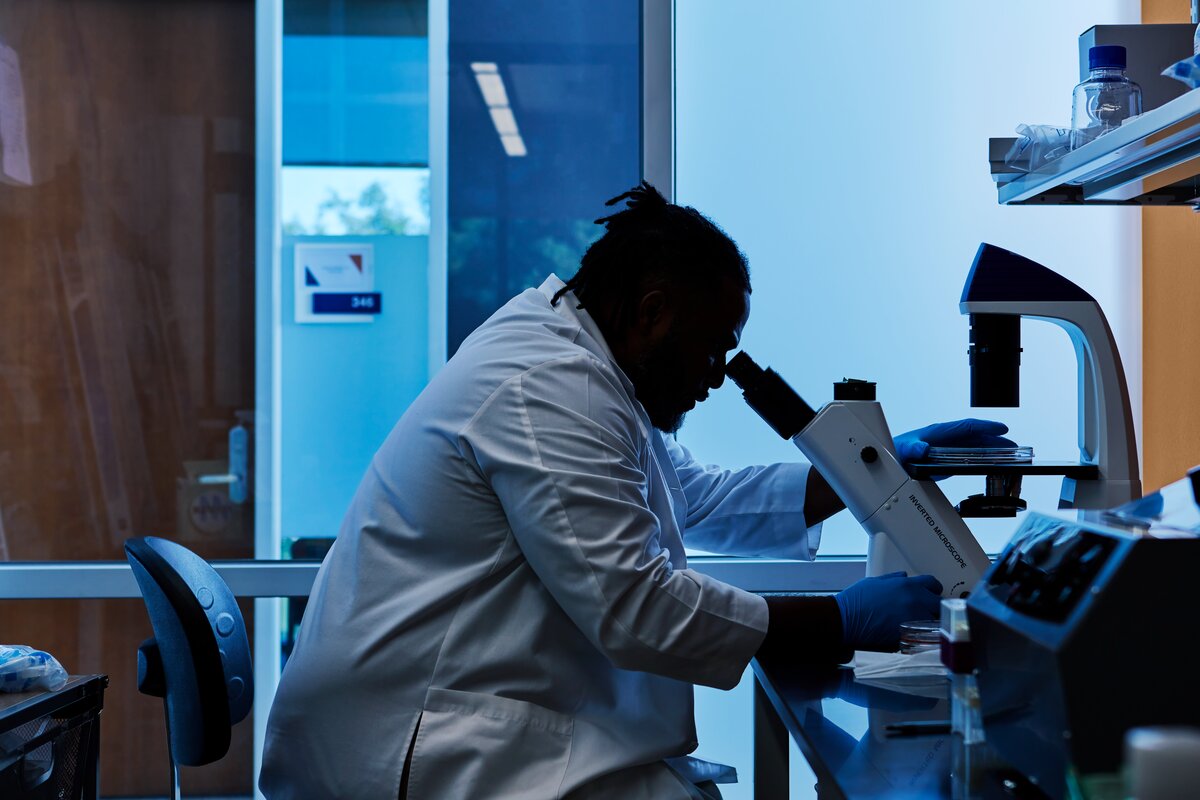 Student in a lab coat looking into a microscope
