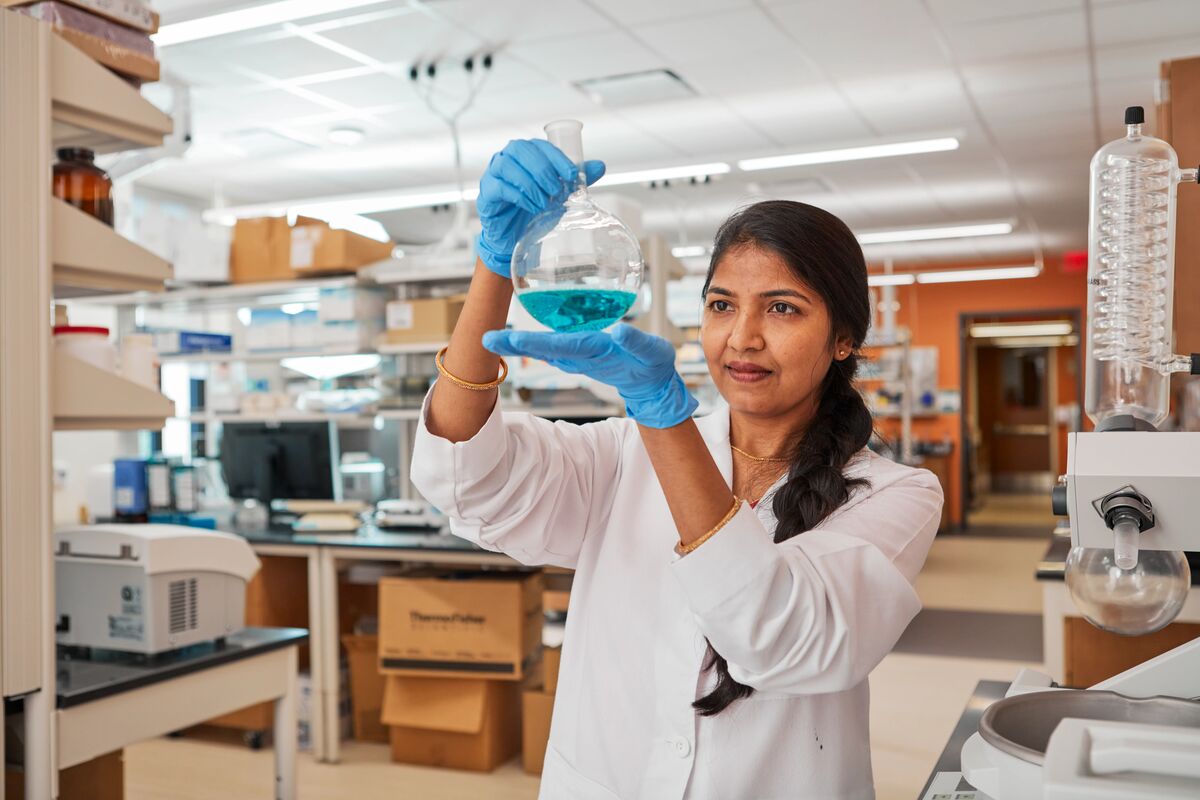 pharmacist holds up vial of blue liquid