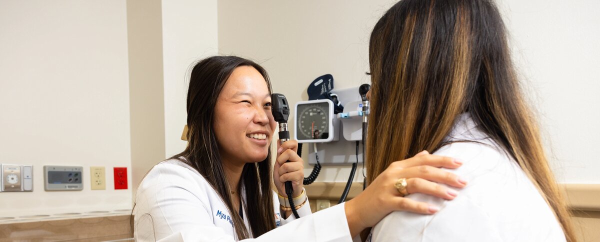 A medicine student looking down a ophthalmoscope at another student