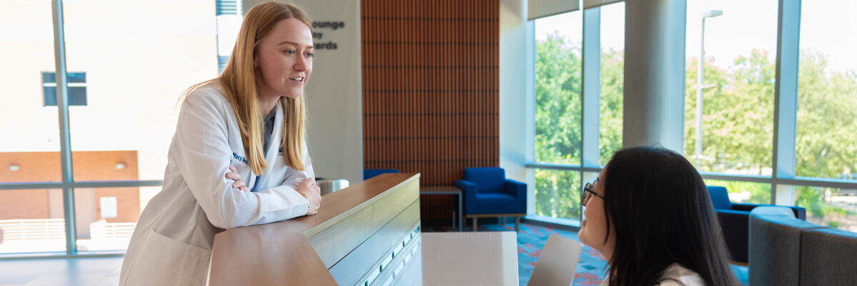 A medicine student talking to another student behind a desk