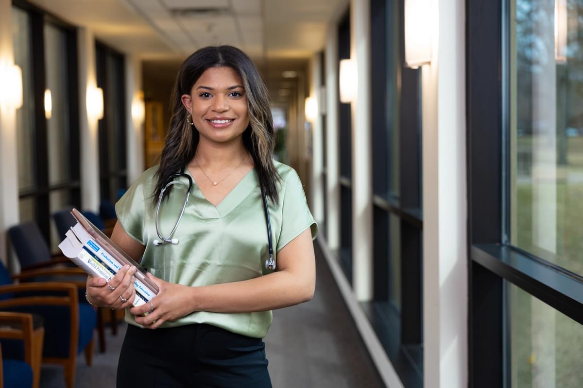 A female UT Tyler nursing student carrying books with a stethoscope around her neck