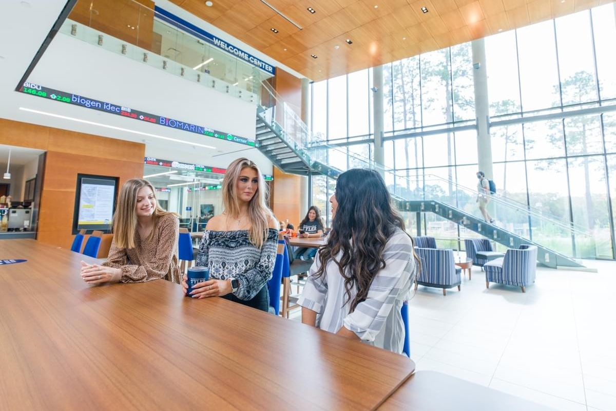 Three female UT Tyler students having a conversation in the lobby of the business school building.