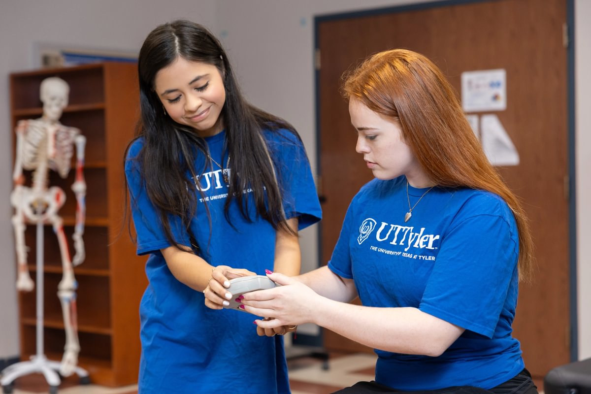 A female student helping another female student use a hand dynamometer