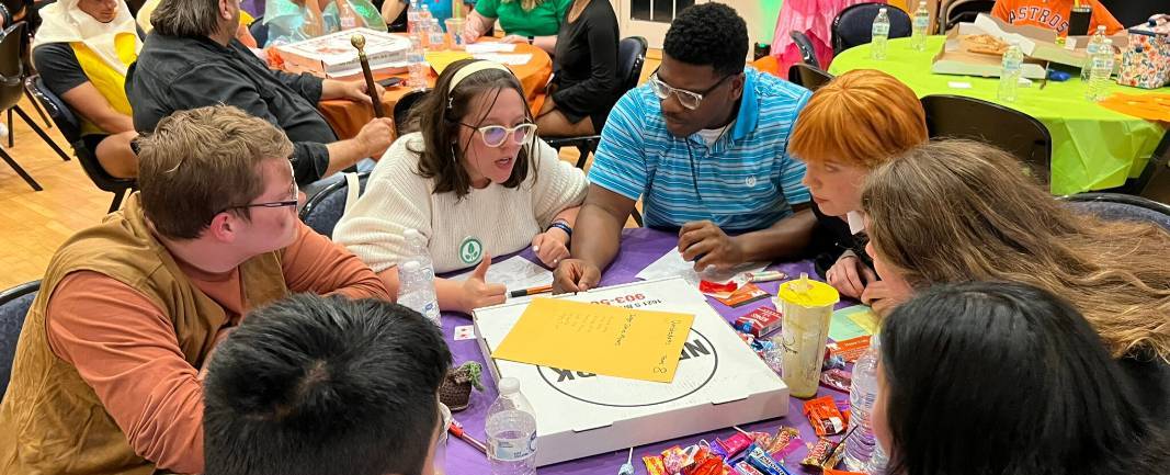Students sitting around a table with a pizza box in the middle