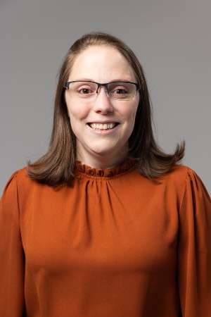 photo of woman in an orange top, wearing glasses, smiling in a photo.