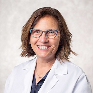 woman wearing white coat, with glasses and smiling. 