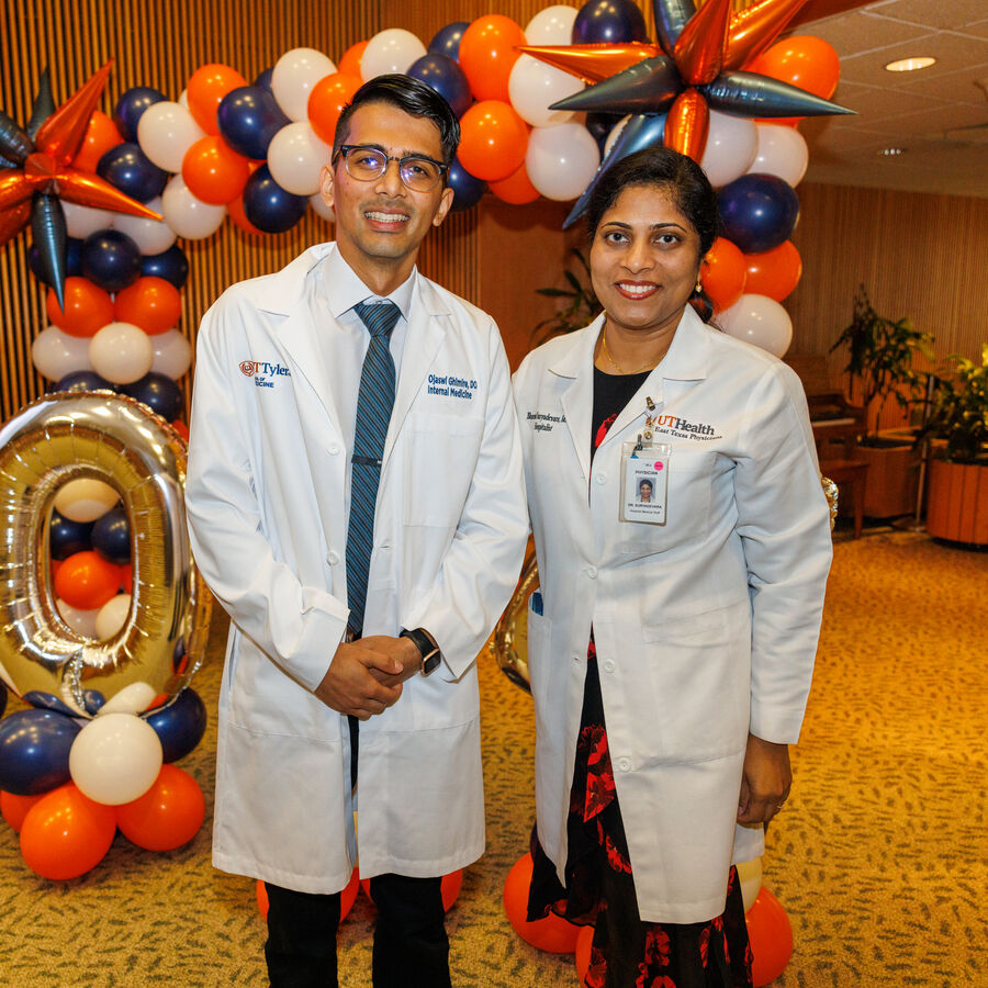Two people in white lab coats in front of colorful balloon decorations