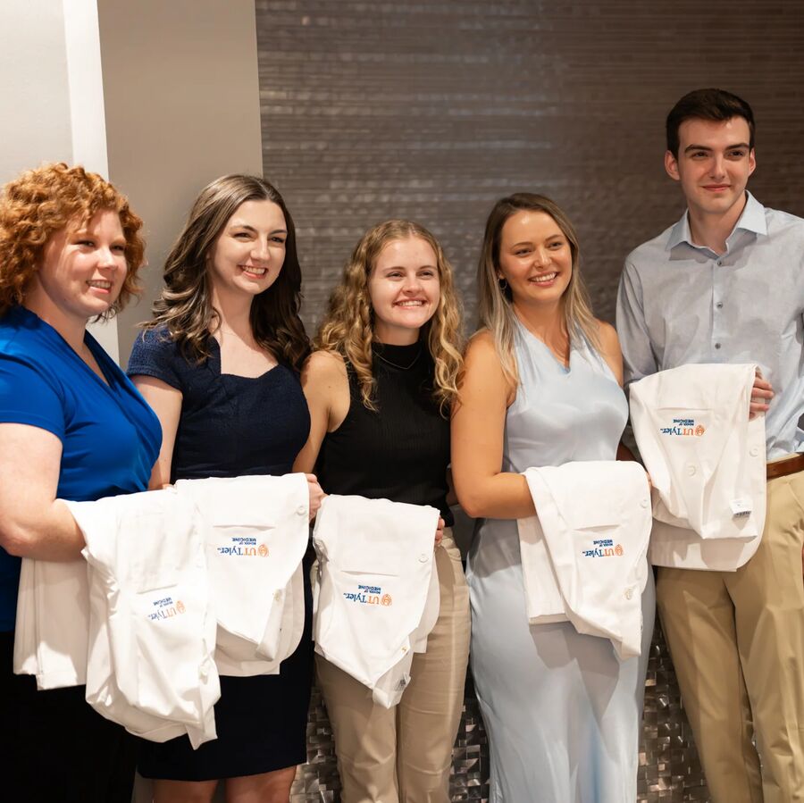 A group of five people posing with folded white coats bearing blue and orange text.