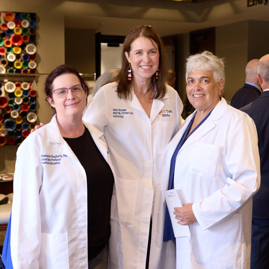 Three people in white lab coats standing together indoors