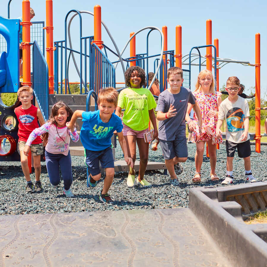 Children running on a playground with colorful equipment.