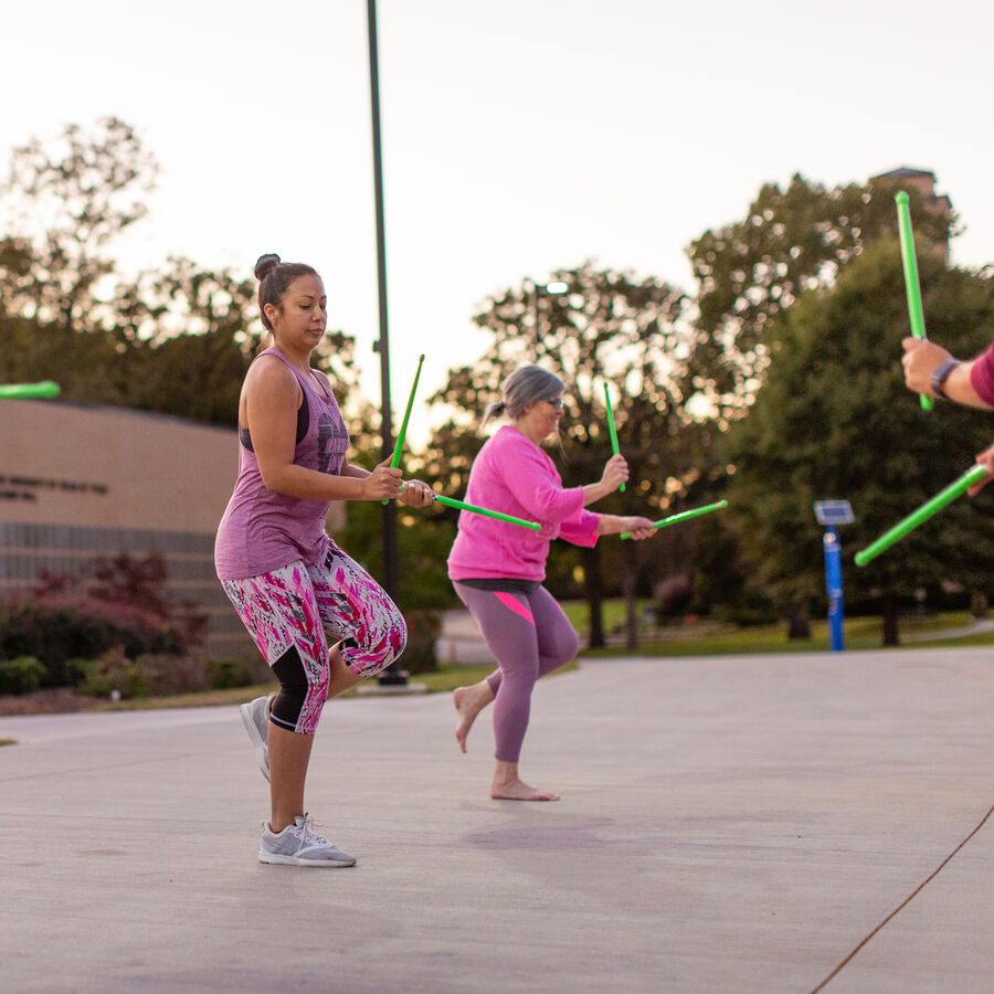 People exercising outdoors with green sticks in a park.