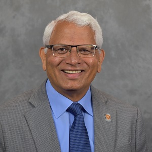man in a grey suit, with blue undershirt, smiling. 