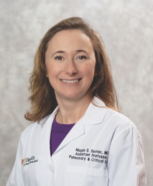 image of woman in a physician coat and purple blouse, smiling.