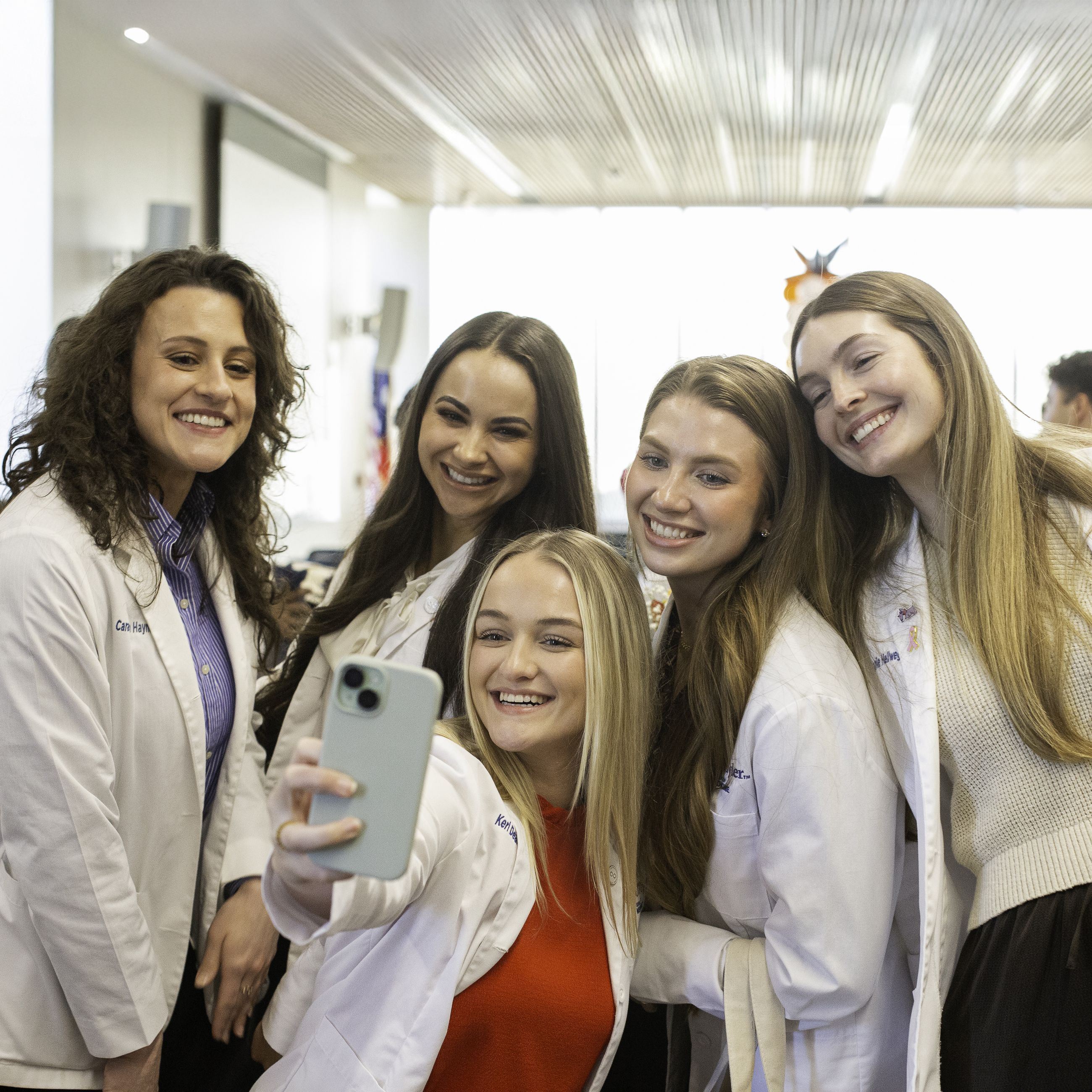 Group of students in white coats smiling while taking a selfie