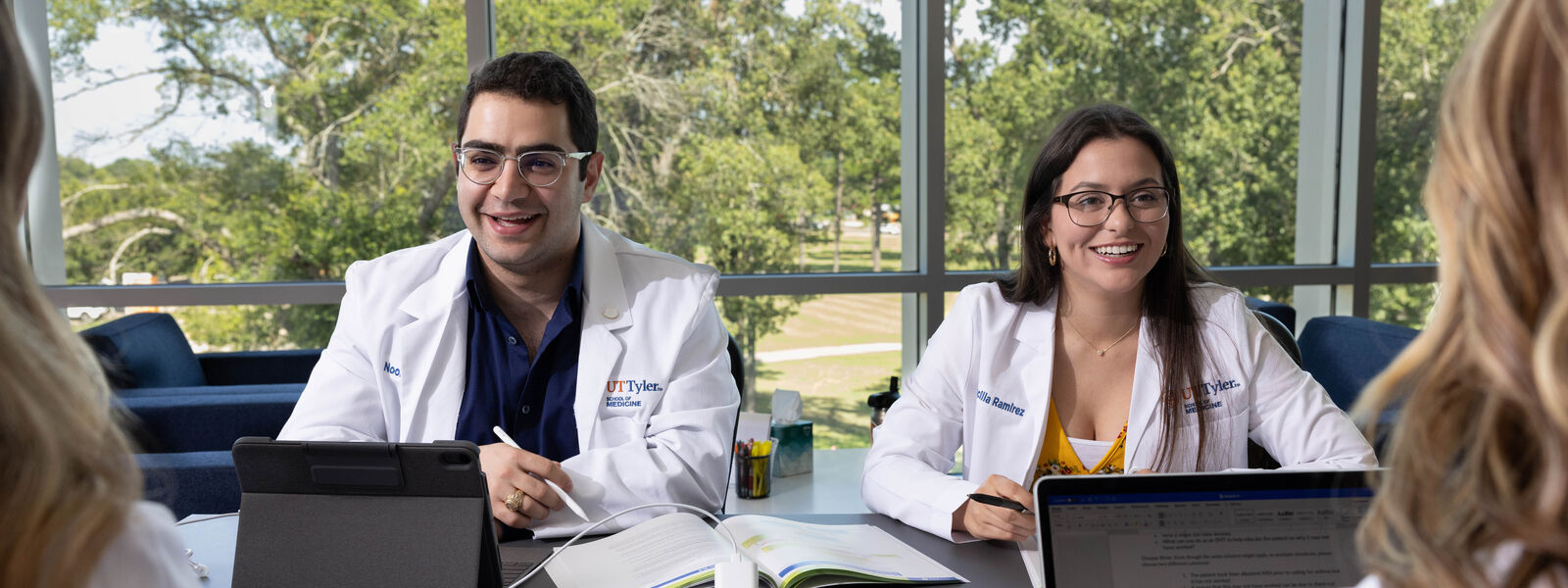UT Tyler School of Medicine students in lab coats sit around a table with laptops
